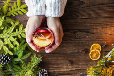 Bir kupa Noel 'le elele tutuşun. Sıcak ve kokulu şarapla, kakule ve tarçınla ahşap bir arka planda..