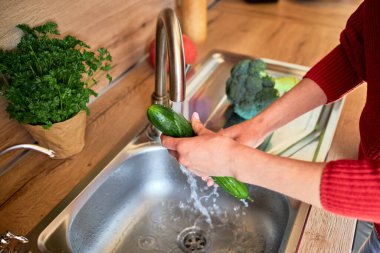 Mutfakta akan musluk suyunun altında sebze yıkayan bir kadının elleri. Yemek pişirme