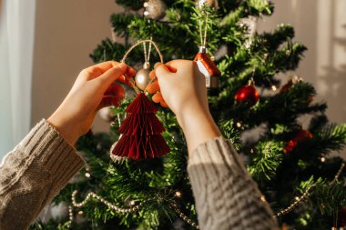 Yılbaşı oyuncağını Noel ağacına asan bir kızın ellerine yakın çekim. Noel ve Yeni Yıl Arifesi.