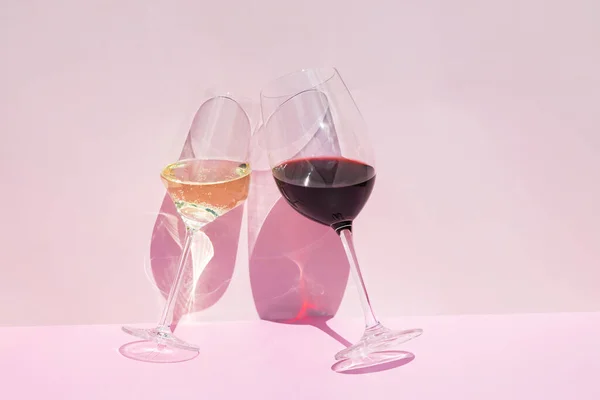 A glass of red and white wine on a pink background in the bright rays of the sun