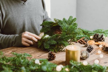 Bir adam evde doğal malzemelerden Noel çelengi yapar. Ekolojik yaşam tarzı. Tatil için kendin yap ev dekorasyonu.