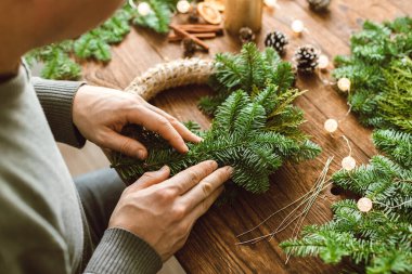 Evde bir adam taze ladin dallarından Noel çelengi yapıyor. Tatil için evini dekore ediyorsun.