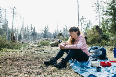 Genç ve güzel bir kadın ormanda yürüyüş yaparken termostan sıcak çay ya da kahve içiyor. Yürüyüş.