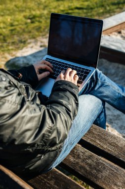 Sokakta dizüstü bilgisayarla çalışan, bankta oturan bir adamın elleri. Uzak çalışma konsepti.