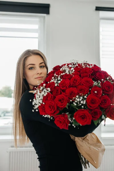 Charming young woman with a huge bouquet of red roses. Flower delivery for holidays and memorable dates.