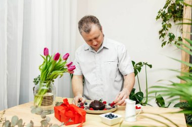 Bir adam çikolatalı keki taze böğürtlen ve çikolatalı kremayla süslüyor. Sevgililer Günü ya da Anneler Günü, Kadınlar Günü için hediye.. 