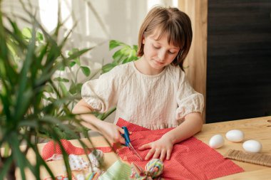 Making Easter eggs in the shape of a hare from textile. The girl prepares the fabric, cuts it with scissors. Home decoration for Easter.