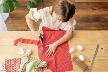 Home decoration for Easter. Top view of a girl who makes eggs from a fabric in the shape of a hare and cuts the fabric with scissors.