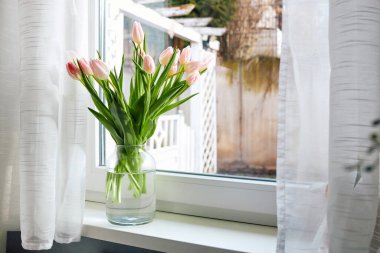 Bouquet of beautiful spring pink tulips in a vase on a windowsill on a sunny day. 