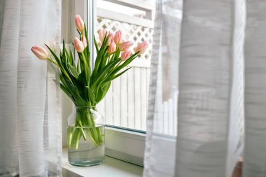 Bouquet of beautiful spring pink tulips in a vase on a windowsill on a sunny day. 