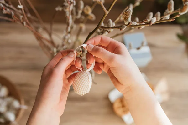 Close-up of a girls hands hanging a decorative Easter egg on a willow branch at home. Decorating your home for Easter.