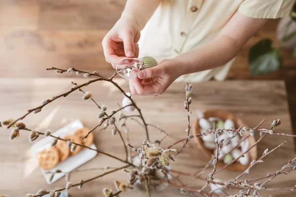 Close-up of a girls hands hanging a decorative Easter egg on a willow branch at home. Decorating your home for Easter.