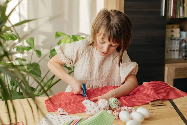 Making Easter eggs in the shape of a hare from textile. The girl prepares the fabric, cuts it with scissors. Home decoration for Easter.