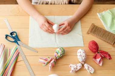 A girl at home makes Easter egg decorations in the shape of a rabbit from fabric. The girls hands wrap the egg in cloth. Ideas for home decoration.