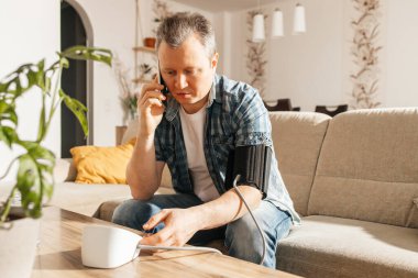 Evde kan basıncını ölçen bir adam tansiyon aleti ve bir tonometreyle ölçer. Adamın biri cep telefonundan doktoru arıyor. Evde sağlık kontrolü. İnternette bir doktora danışıyorum..