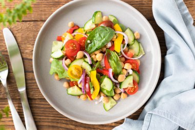 Nohut, domates, kırmızı soğan, salatalık ve marullu vejetaryen sebze salatası. Protein ve lif açısından zengin vejetaryen yemekleri. Sebze salatası ahşap masa manzaralı.. 