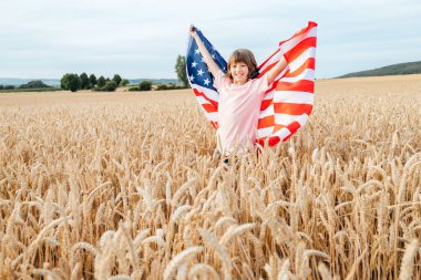 Buğday tarlasında Amerikan bayrağı taşıyan mutlu kız. Çocukların özgürlüğü ve vatanseverliği. 4 Temmuz Bağımsızlık Günü. 