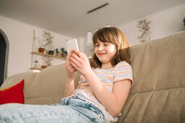 stock image A teenage girl sits on the couch at home and uses a mobile phone, chatting and calling friends. Teenagers and technology. 