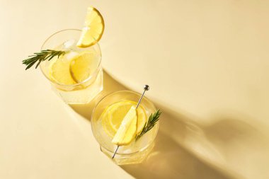 Gri bir masanın üzerinde biberiye filizi ile süslenmiş taze limonla ferahlatıcı yaz içecekleri. Limonlu alkollü kokteyller.