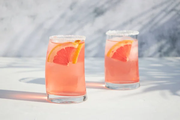 フレッシュで冷たい夏のグレープフルーツとアイスカクテル 新鮮なフルーツスライス付きの2つのグラス 赤オレンジドリンク 晴れた日の影 — ストック写真