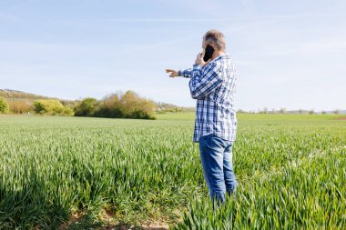 Erkek bir çiftçi tarlada duruyor ve telefonda konuşuyor. Tarım alanında modern teknolojiler. 
