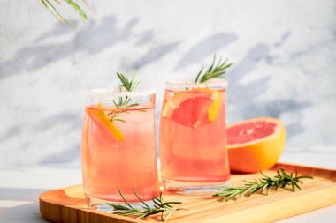 Güneşli bir günde, gri bir arka planda, ahşap servis tepsisinde soğuk greyfurt ya da kırmızı portakal, biberiye ve buz kokteyli. Tatil kavramı