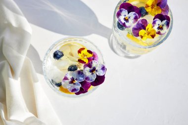 Parlak güneş ışınlarında turunçgiller ve yenilebilir çiçeklerle ferahlatıcı bir kokteylin üst görüntüsü. Yaz ferahlatıcı içecekler