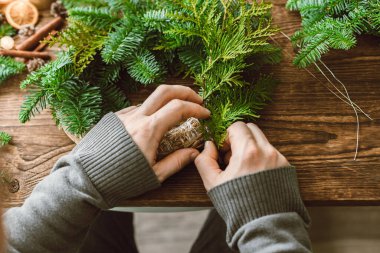 Bir adam doğal çevre dostu malzemelerden Noel süsü yapar. Erkek bir çiçekçinin çelenk üzerindeki çelenk dallarını tamir ettiği yakın plan.