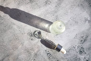 Kozmetik sıvıyla dolu bir şişe ve yanında gri beton arka planda bir pipet.. 