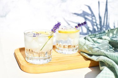 Limonlu ve buzlu soğuk lavantalı limonata gri bir masada ahşap bir standın üzerinde. Diyet alkolsüz yaz kokteyli. Limonlu detoks suyu. 
