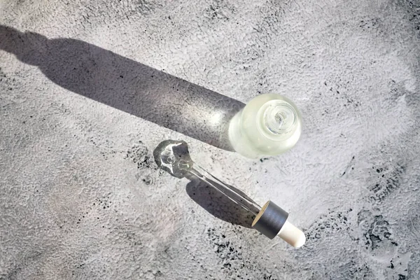 Kozmetik sıvıyla dolu bir şişe ve yanında gri beton arka planda bir pipet.. 