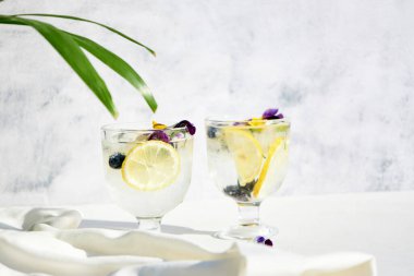 Yenilebilir çiçeklerle süslenmiş limonlu soğuk su. Serin yaz limonatası. Alkolsüz yaz kokteylleri ve içkileri