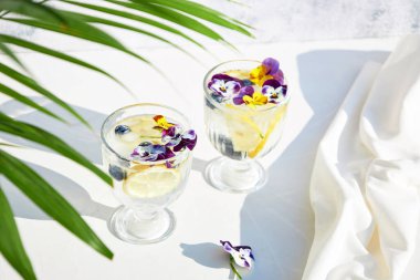 Yenilebilir çiçeklerle süslenmiş limonlu soğuk su. Serin yaz limonatası. Alkolsüz yaz kokteylleri ve içkileri