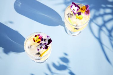 Parlak güneş ışınlarında turunçgiller ve yenilebilir çiçeklerle ferahlatıcı bir kokteylin üst görüntüsü. Yaz ferahlatıcı içecekler