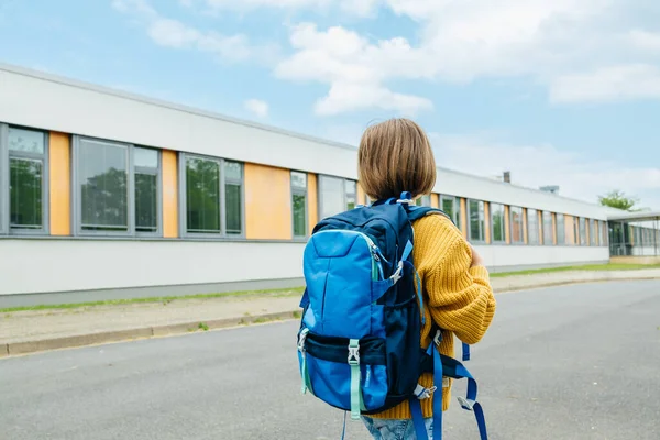 stock image A view from the back of a girl with a school bag on her back is standing next to the school building. Beginning of the school year.