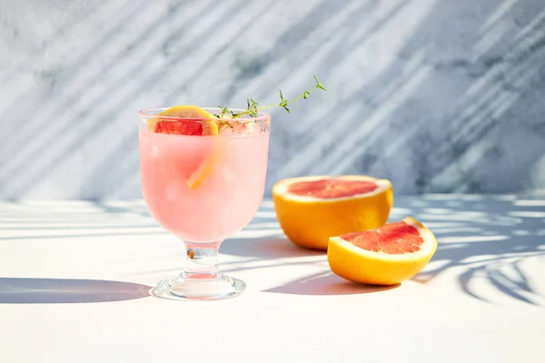 A chilled drink with grapefruit or red orange in glasses on a gray background under the shadow of palm leaves. Summer soft drinks and cocktails with fresh fruit.