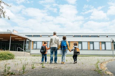 Back to school. A father walks his children to school. Beginning of the school year. Parental care for children