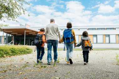 Back to school. A father walks his children to school. Beginning of the school year. Parental care for children