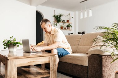 Evde dizüstü bilgisayarla çalışan başarılı, mutlu bir serbest yazar. Adamın biri kanepede oturup internetten alışveriş yapmak ve iletişim kurmak için dizüstü bilgisayar kullanıyor..