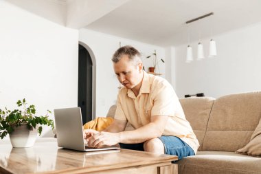 Evde dizüstü bilgisayarla çalışan başarılı, mutlu bir serbest yazar. Adamın biri kanepede oturup internetten alışveriş yapmak ve iletişim kurmak için dizüstü bilgisayar kullanıyor..