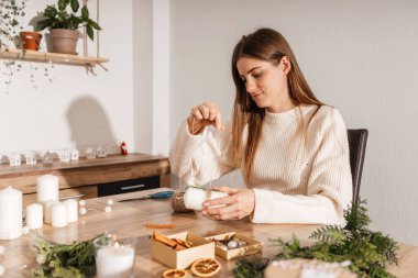 Genç bir kadın evinde kendi elleriyle yılbaşı süsü istiyor. Bir kız Noel süsü, tarçın çubukları ve taze yeşil dallarla el yapımı mumlar süslüyor. Yeni yılı bekliyorum.