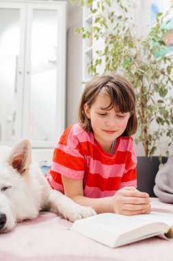 Genç bir kız odasında yerde köpeğinin yanında bir kitap okuyor. Beyaz İsviçreli bir çoban. Hobi olarak kitap okumak..