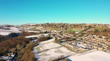 Aerial drone footage of the village of Golcar in West Yorkshire, England, Huddersfield in the UK showing the residential houses estates in the winter time with small patches of snow on the ground.