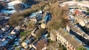 Aerial drone footage of the village of Golcar in West Yorkshire, England, Huddersfield in the UK showing the residential houses estates in the winter time with small patches of snow on the ground.