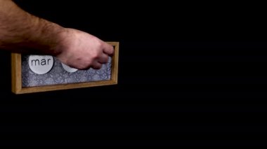 A wooden calendar block showing the date March 9th with a mans hand putting on and taking off the metal discs with the date and month on them, filmed in 8k quality