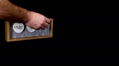 A wooden calendar block showing the date March 12th with a mans hand putting on and taking off the discs with the date and month on then, filmed in 8k quality