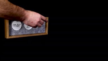 A wooden calendar block showing the date March 27th which is Mothering Sunday mothers day with a mans hand putting on and taking off the metal discs with the date month on them, filmed in 8k quality