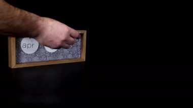 A wooden calendar block showing the date April 2nd with a mans hand putting on and taking off the metal discs with the date and month on them, filmed in 8k quality.