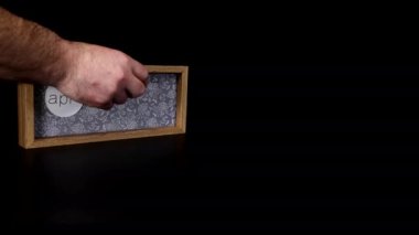 A wooden calendar block showing the date April 8th with a mans hand putting on and taking off the metal discs with the date and month on them, filmed in 8k quality.