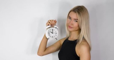 An attractive blonde haired woman holding up an old style alarm clock that is set to 10 o'clock, waking up at 10am or 10pm concept.